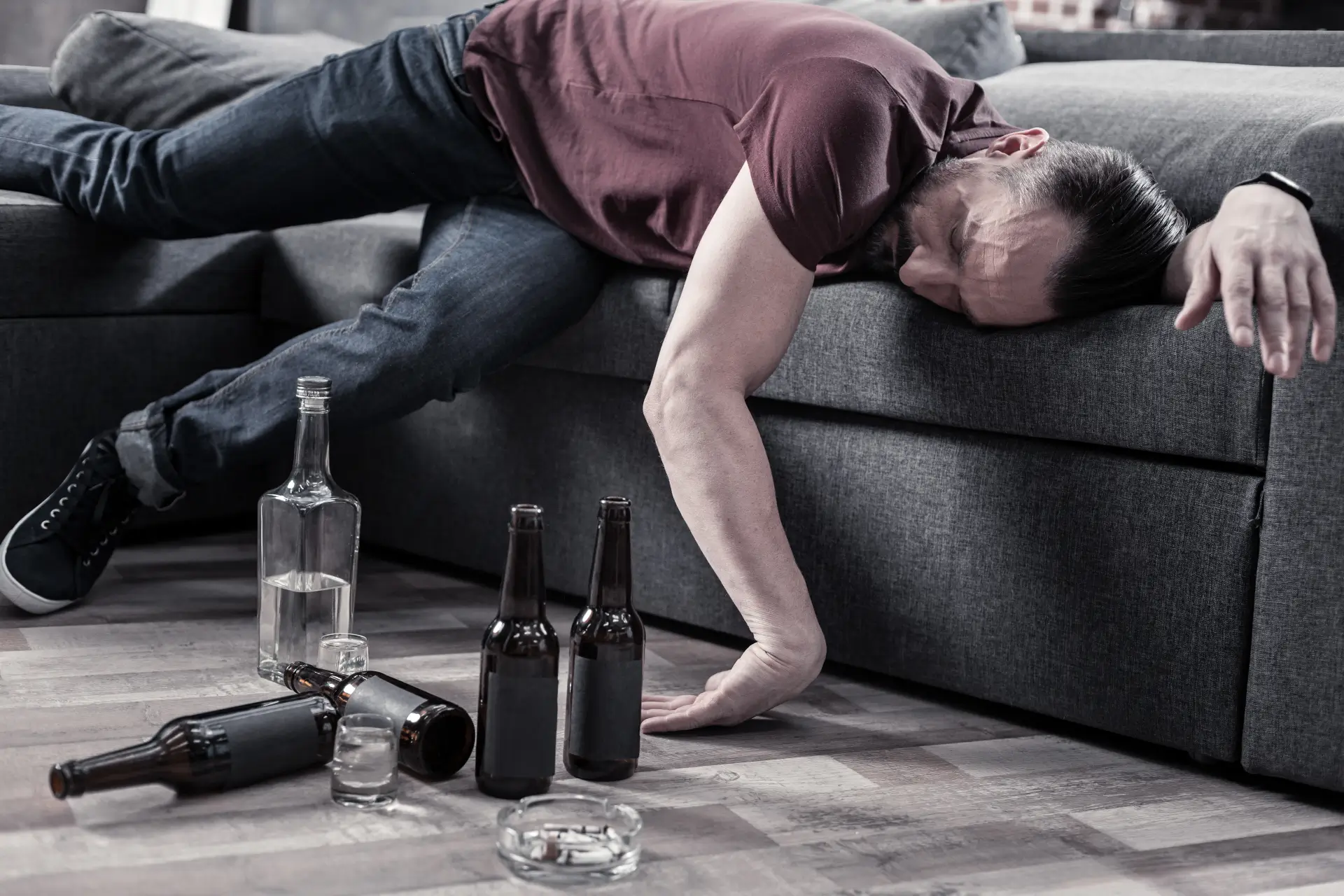 man half lying on a couch surrounded by beer bottles